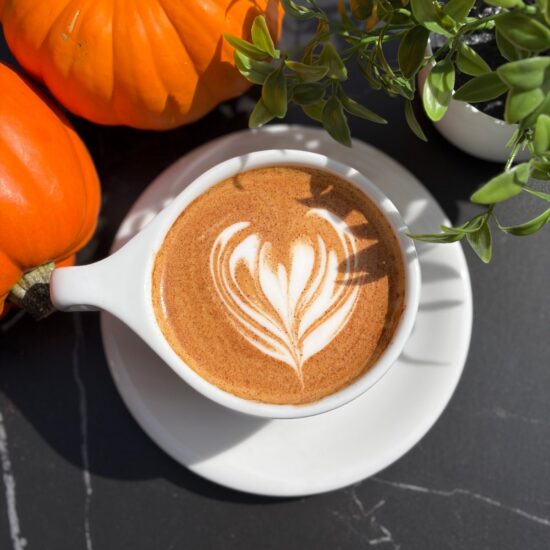 Pumpkin spice latte with heart latte art next to pumpkins at Frenchies Coffee Bar